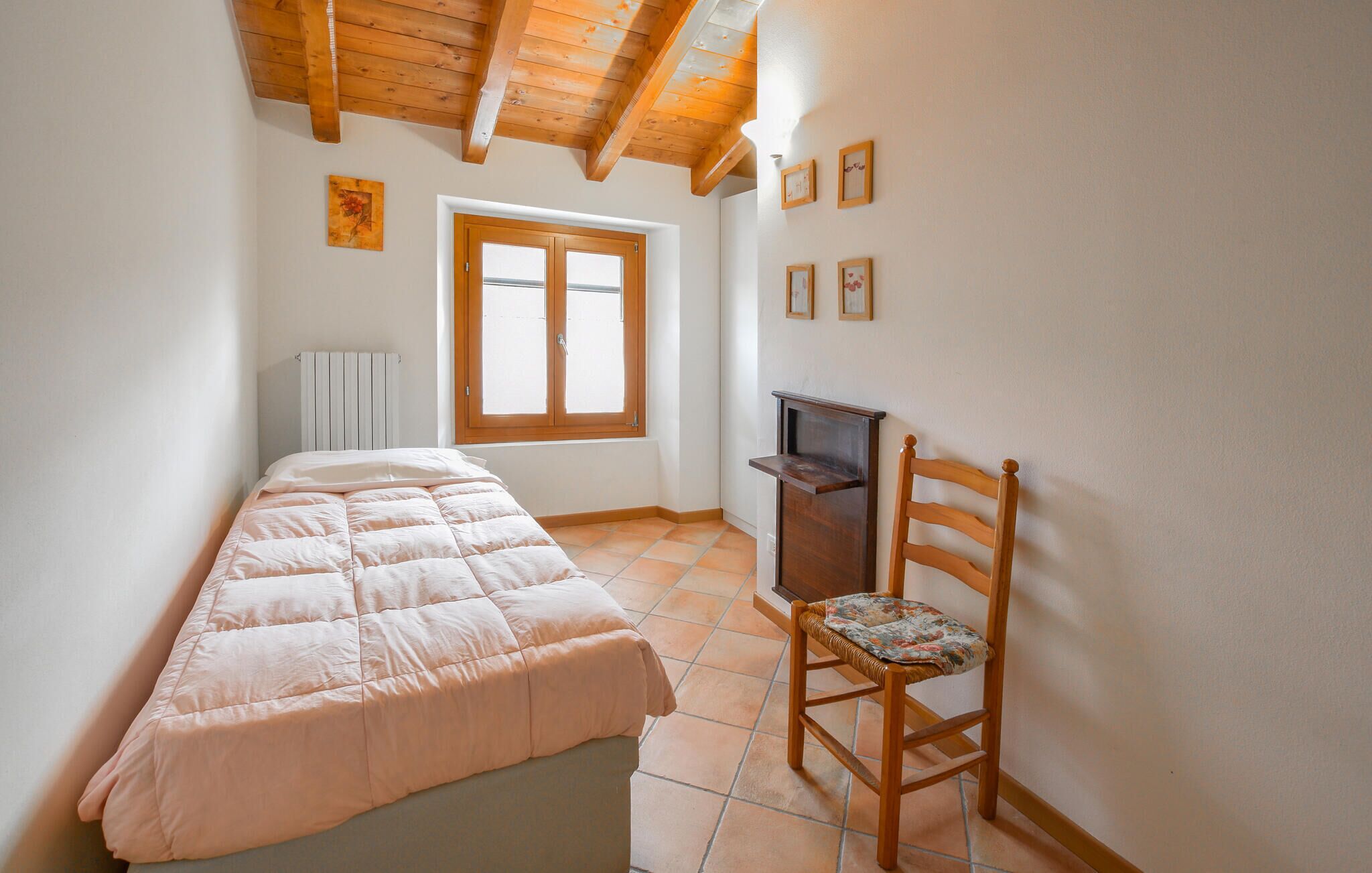 Une chambre à coucher avec un lit, une chaise en bois, un radiateur, une fenêtre et un plafond en bois.