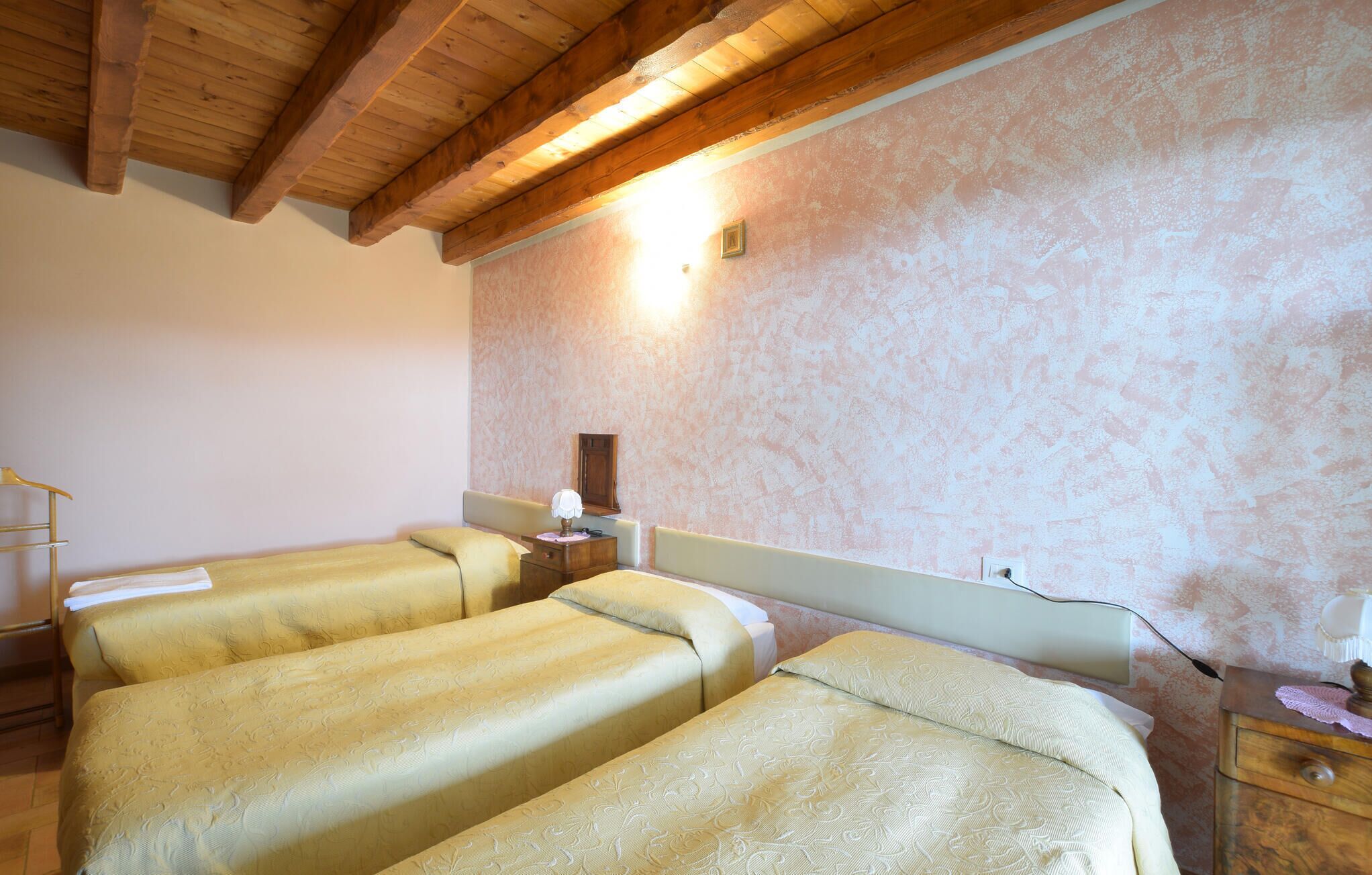 Una habitación con dos camas, vigas de madera en el techo, una lámpara fijada a la pared y una mesita de noche de madera.