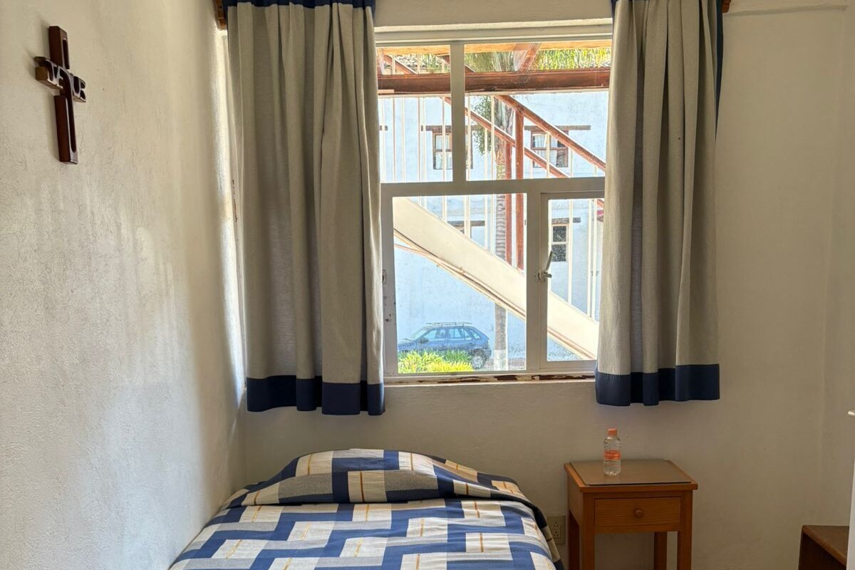 Un dormitorio con cama, mesita de noche, ventana con cortinas y una escalera en el exterior.