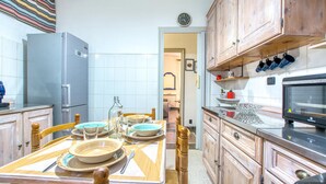 A kitchen with wooden cabinets, a refrigerator, a dining table set with plates and bowls, and a television on the counter. - 1 bedroom nice apartment in Genova (Genova)