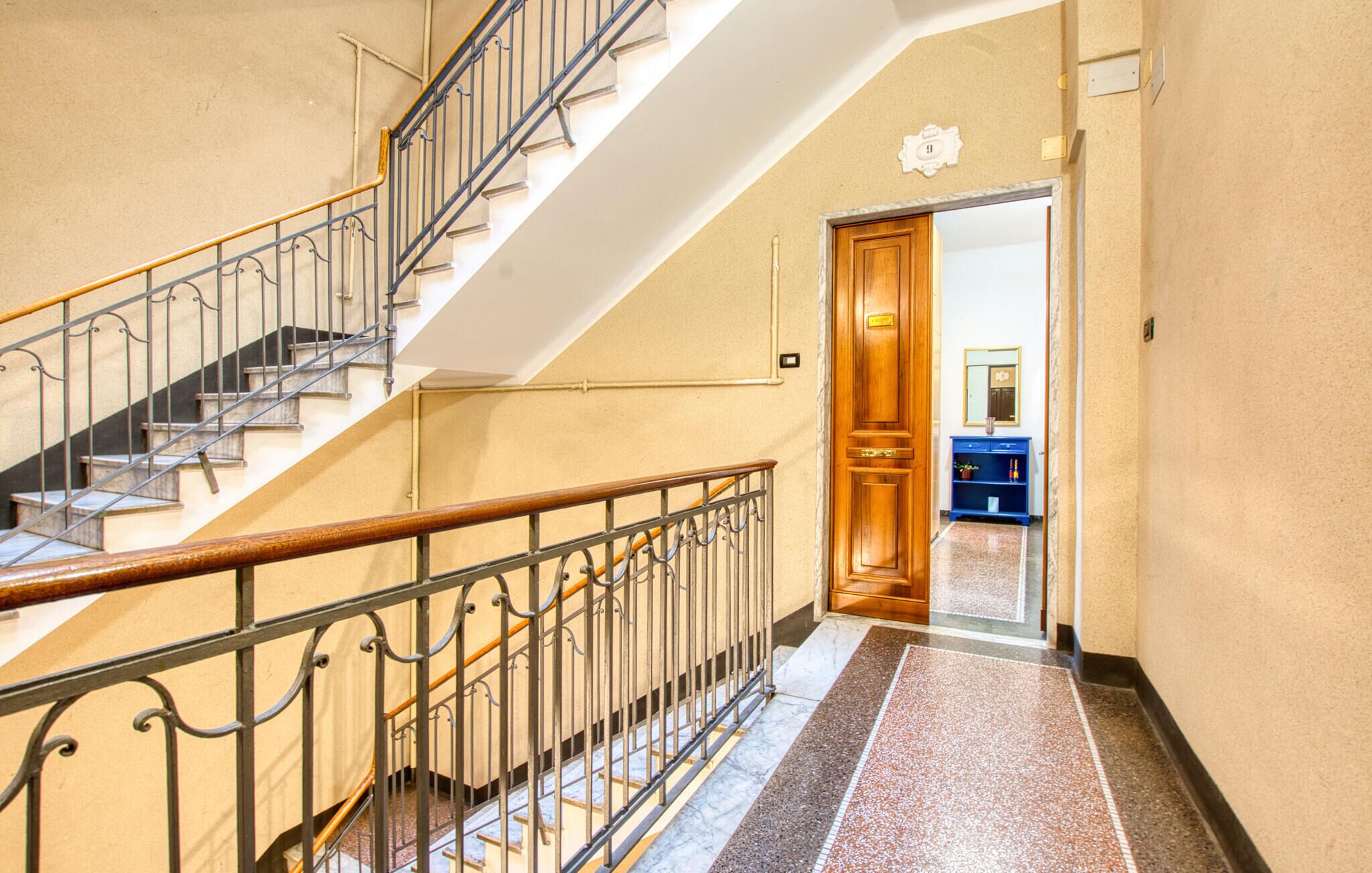 A staircase with a wooden handrail and metal balusters, leading to a room with a wooden door and a blue cabinet.