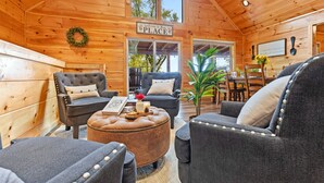 A cozy cabin interior with wooden walls, a 'Welcome to Place E' sign, and a dining area with a table and chairs. - The Great Smoky Haven (Sevierville)