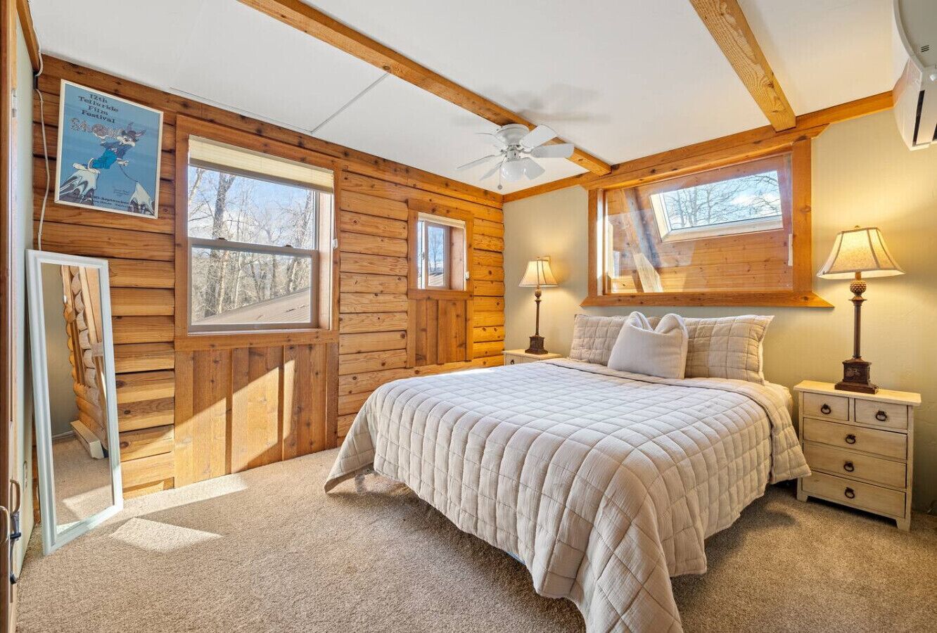 A bedroom with a bed, two bedside tables, a ceiling fan, and wooden walls.