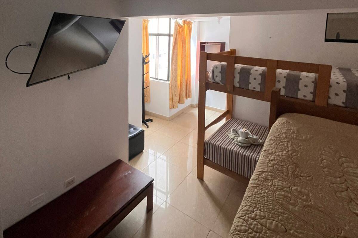 A bedroom with a bed, a bench, a TV mounted on the wall, and a ceiling light.