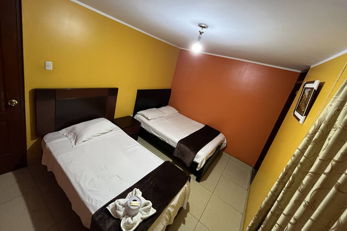 A hotel room with two beds, a ceiling fan, and a window with curtains.