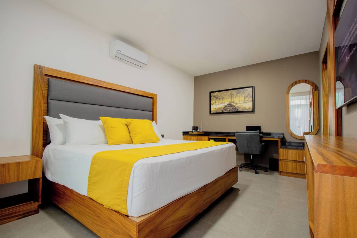 A hotel room with a large bed, a desk, a chair, a mirror, and a small table.
