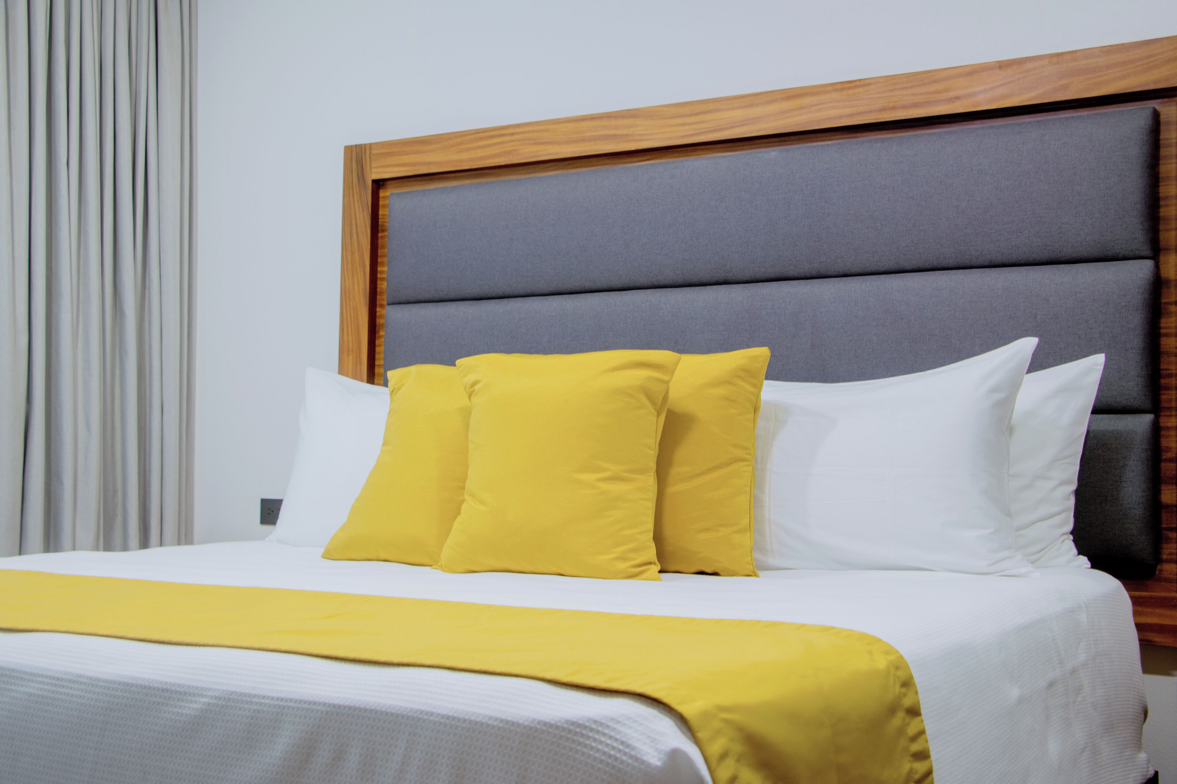 A neatly made bed with white and yellow bedding, a wooden headboard, and a grey upholstered headboard section.