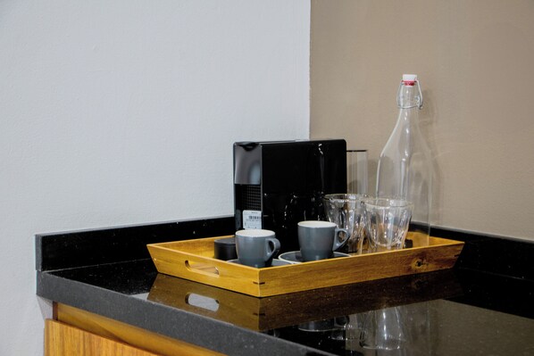 A tray with a coffee maker, cups, and a bottle on a kitchen counter.