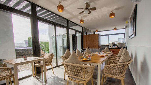 A modern dining area with wicker chairs, a wooden table, and large windows offering a view of the cityscape. - LF Hotel Boutique (Playa del Carmen)