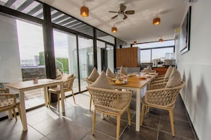 A modern dining area with wicker chairs, a wooden table, and large windows offering a view of the cityscape.