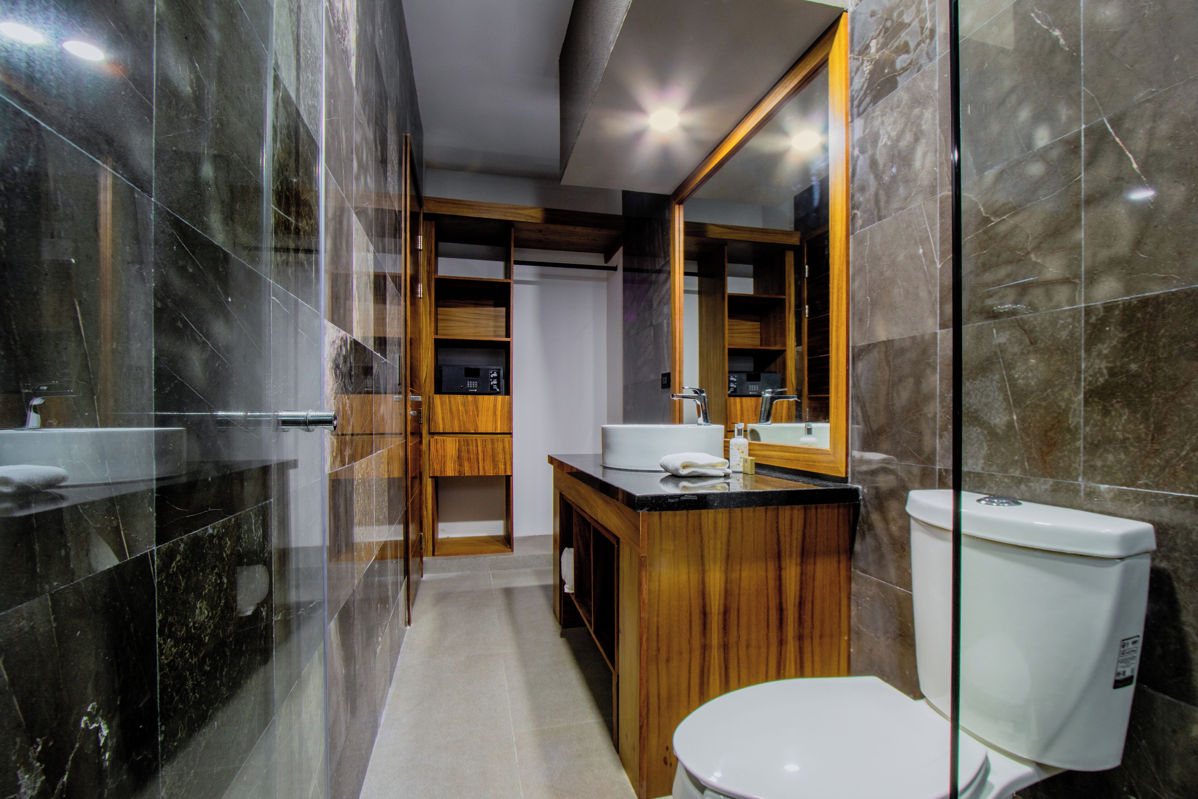 A modern bathroom with a glass shower enclosure, a wooden vanity, a white toilet, and a large mirror.