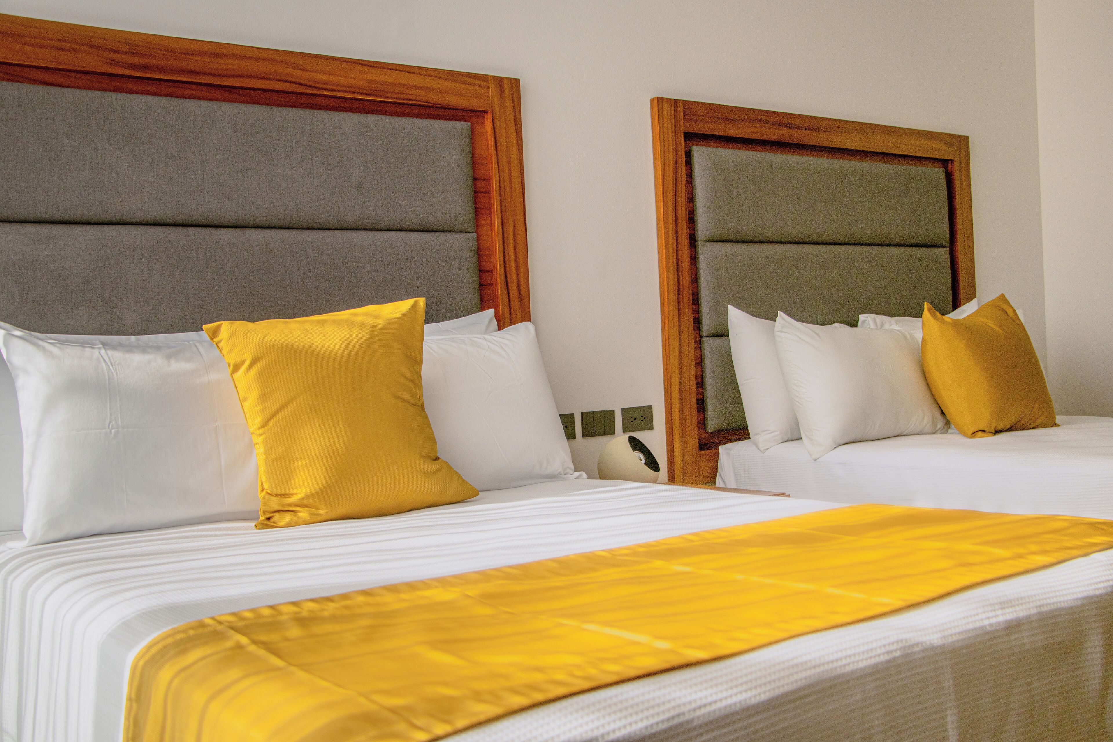 Habitación de hotel con dos camas, cada una con cabecero de madera, ropa de cama blanca y almohadas amarillas.