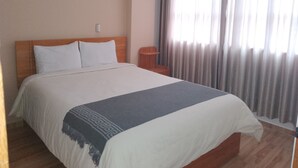 Une chambre d’hôtel avec un grand lit, une tête de lit en bois, une table de chevet et une fenêtre avec des rideaux.