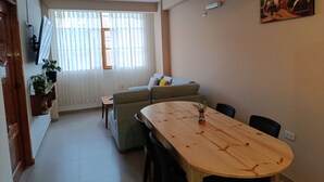 Un coin repas comprenant une table en bois, des chaises, un canapé et une fenêtre ornée de rideaux légers.