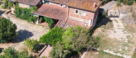 An aerial view of a house with a tiled roof, surrounded by greenery and a stone pathway.