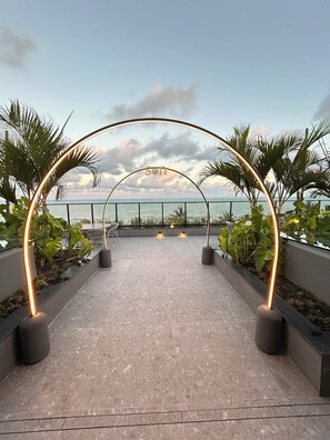 An outdoor pathway with a metal archway and illuminated lights, leading to a view of the sea. - Melhores Flats - Conforto à beira-mar (Cabedelo)