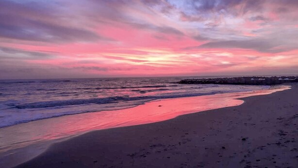 Ein Strand mit Sonnenuntergang, Wellen und einer fernen Küste.