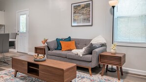A modern living room with a grey sofa, wooden coffee table, and a side table with a vase. A framed picture hangs on the wall, and a lamp is on the side table. - Magic City Manor: Groups/Driveway/Game Room/Wifi (Birmingham)