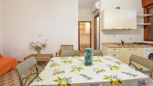 Una cocina compacta con gabinetes blancos, una estufa y un lavamanos. Hay una mesa de comedor con mantel estampado y sillas.
