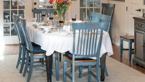 Comedor con candelabro, sillas azules, mantel blanco y un jarrón de flores.
