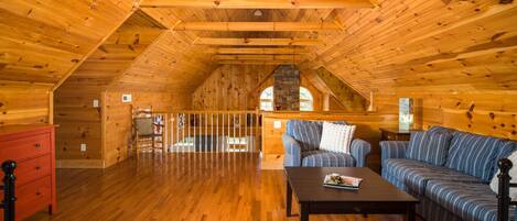 L’intérieur d’une cabane en rondins, avec un plancher en bois, un canapé, une table et une commode rouge.
