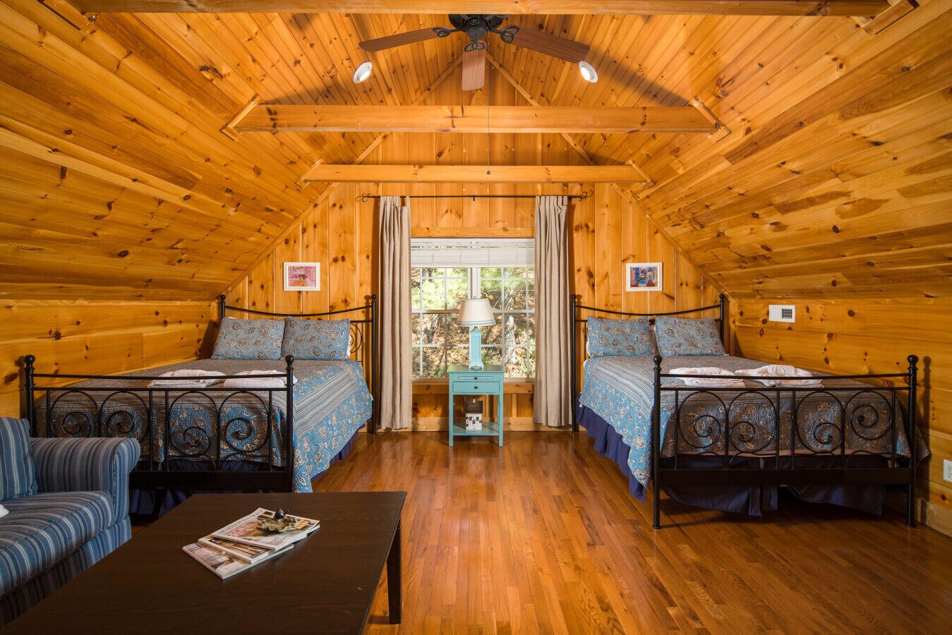 A cabin with two beds, a wooden ceiling, and a window with curtains.