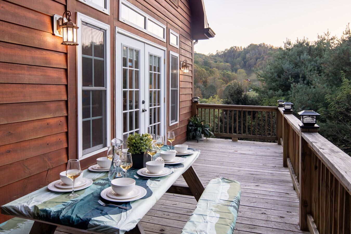 A wooden deck with a dining table set for four, overlooking a forested area.
