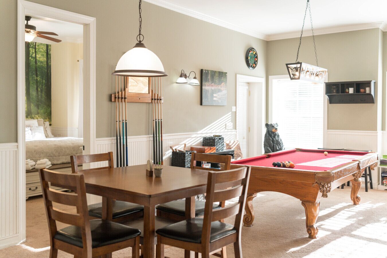Une table de billard dans une pièce qui contient également une table à manger et des chaises, une horloge au mur et une statue d’ours.