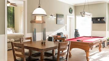 Une table de billard dans une pièce qui contient également une table à manger et des chaises, une horloge au mur et une statue d’ours.