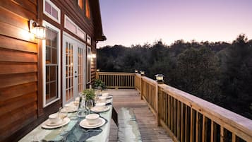 A wooden deck with a table set for dining, overlooking a forested area.
