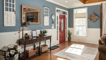 A room with a wooden console table, a red door, a large window, and a decorative wall piece.