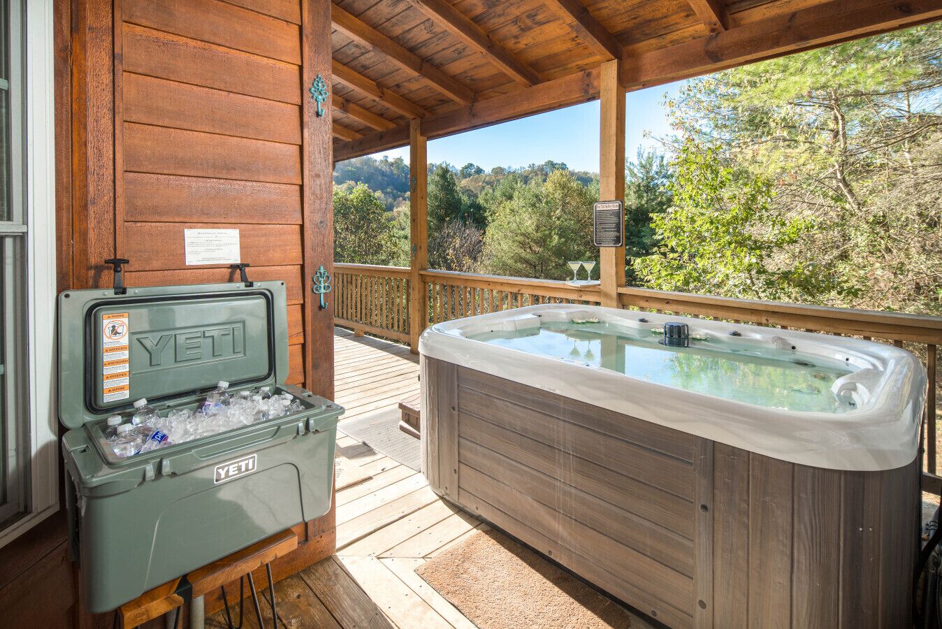 A wooden cabin with a hot tub and an ice chest on the deck.