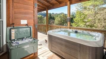 A wooden cabin with a hot tub and an ice chest on the deck.