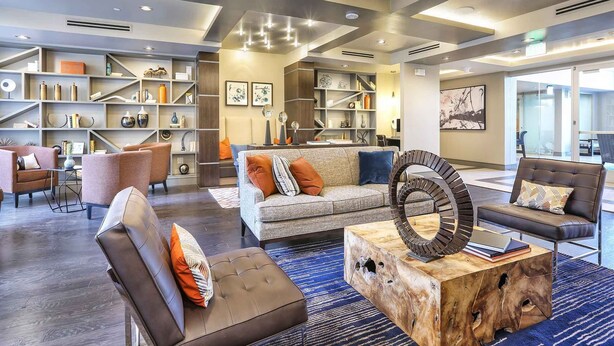 En rymlig entréhall med modern design, med en stor sittgrupp bestående av soffor och fåtöljer, ett träbord och en bokhylla fylld med böcker och dekorativa föremål.