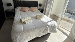 A modern hotel room with a large bed, two bedside tables with lamps, a window with curtains, and a cityscape view.
