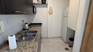 A compact kitchen with dark cabinets, a granite countertop, a stainless steel sink, and a white refrigerator.