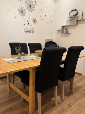 A dining area with a wooden table, black chairs, a small plant, and a wall decal of dandelions.