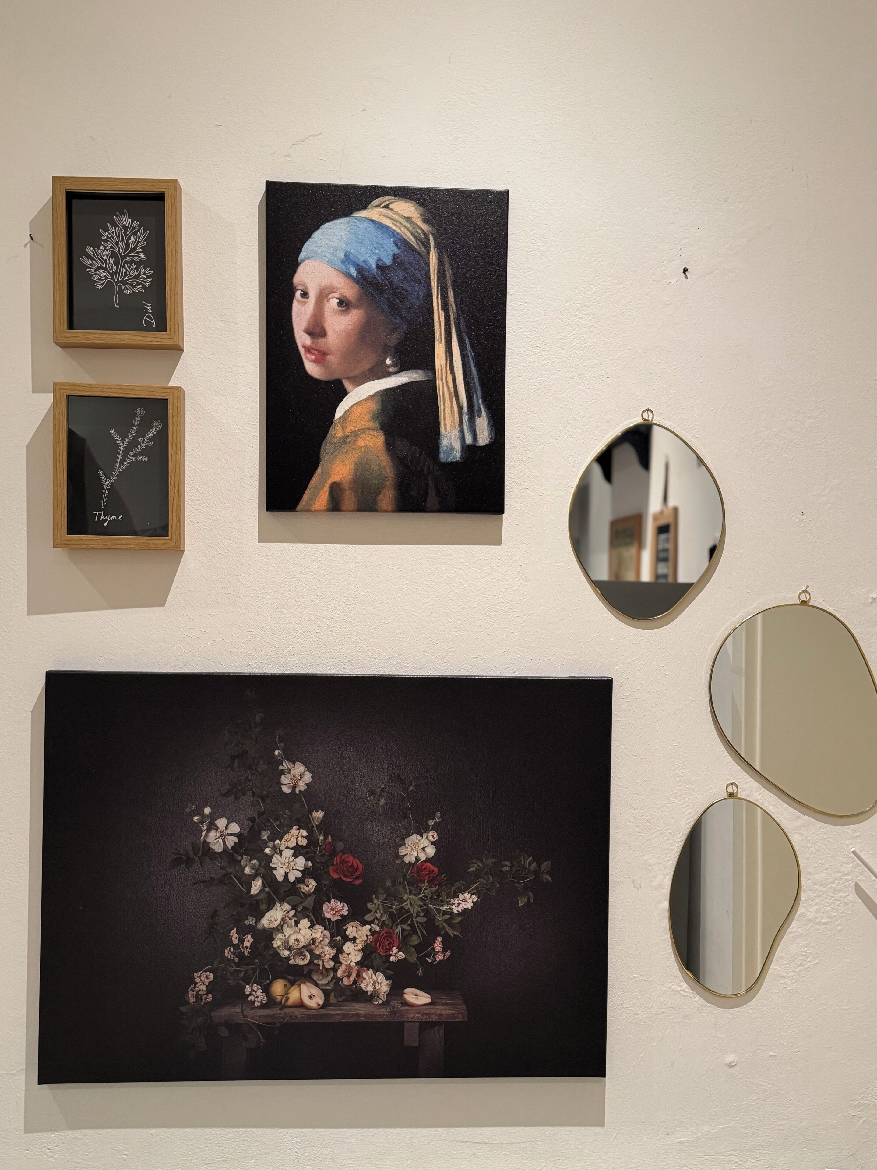 A wall with three framed artworks, a large painting, and three mirrors.