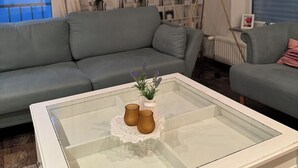 A living room with a grey sofa, a glass coffee table with decorative items, a bookshelf, and a floor lamp.