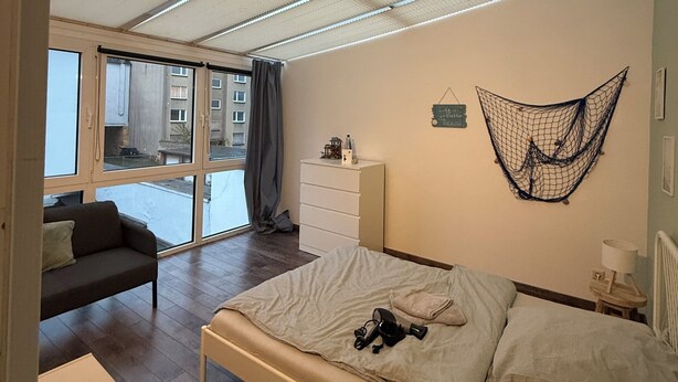 A bedroom with a bed, a dresser, a hanging net decoration, and a view of the outside.