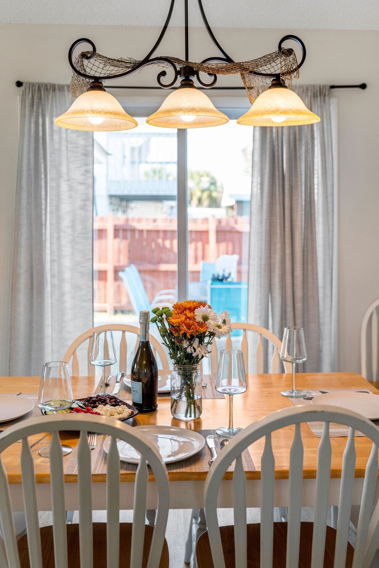 A dining table set with chairs, a vase of flowers, wine glasses, and a bottle of wine.