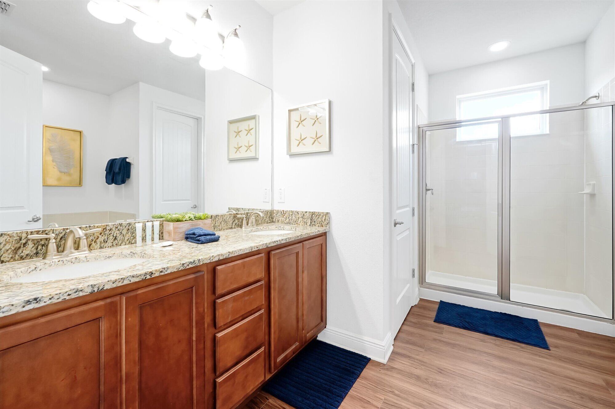 A bathroom with a marble countertop, wooden cabinets, a large mirror, and a glass shower enclosure.
