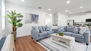Un salon moderne avec un canapé d’angle gris, une table basse et une grande plante en pot.
