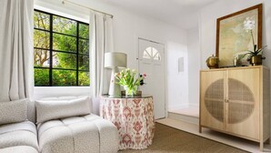Una habitación con un sofá, una mesa redonda con mantel estampado, un aparador con un globo terráqueo y una ventana con cortinas.