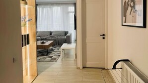 Un salon moderne avec un canapé, une table basse et un téléviseur. Un couloir mène à une chambre dotée d’une porte et d’un radiateur.