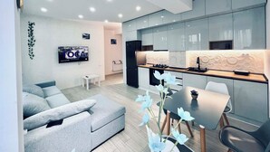 Un salon moderne avec un canapé gris, une petite table blanche et un téléviseur fixé au mur.