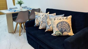 Ein Wohnzimmer mit einem dunkelblauen Sofa, einem Esstisch mit Stühlen und einem Wandbild mit einer Strandansicht.
