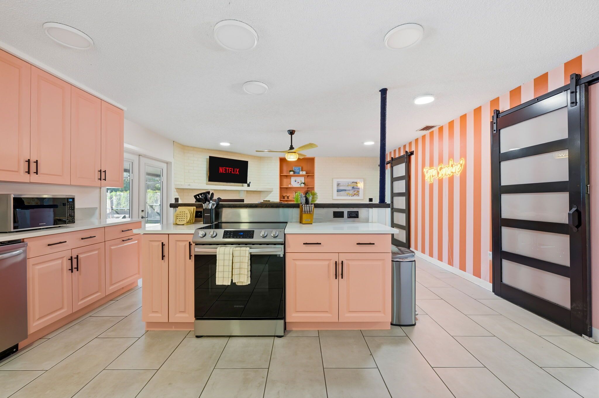 A modern kitchen with pink cabinets, a black oven, a microwave, and a neon sign on the wall.