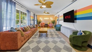 Ein Wohnzimmer mit Sofa, Sesseln, Couchtisch und an der Wand montiertem Fernseher.