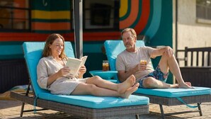 Zwei Personen entspannen in Liegestühlen am Pool, lesen und trinken.